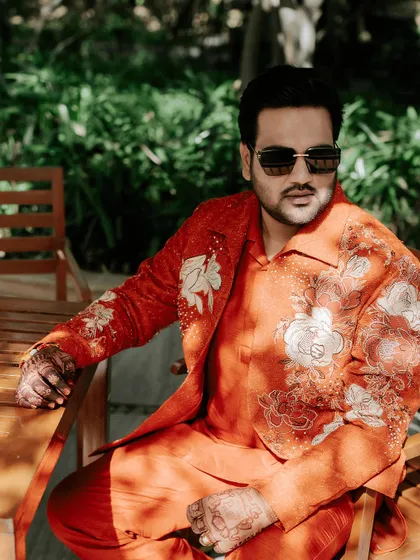 The groom looking dapper in his embroidered orange jacket, a perfect modern-ethnic look for a daytime carnival event.