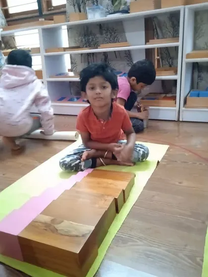Here, a child works with the Brown Stairs and Pink Tower. These classic sensorial materials help children understand dimensions, weight, and size relationships, laying a foundation for future math and geometry work.