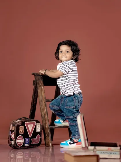 A cool toddler posing on a stepladder with a vintage suitcase. We love creating unique and stylish portraits.