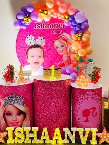 A glamorous Barbie-themed party for Ishaanvi's first birthday. The decor is all about pink glitter, with Barbie cutouts, themed pedestals, and a photo of the birthday girl.