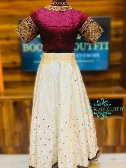 This is a custom-stitched lehenga perfect for a reception or sangeet. It pairs a rich maroon brocade blouse with short, embroidered sleeves and a simple off-white skirt with scattered motifs, creating a balanced and elegant look.