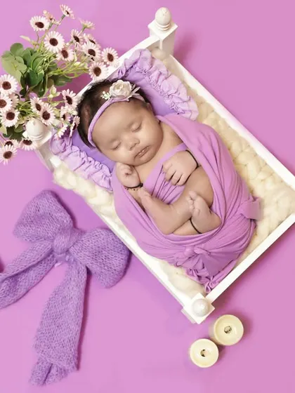 We style our newborn sessions with coordinating props, like this lavender bow and floral arrangement, to create a cohesive and aesthetically pleasing portrait.