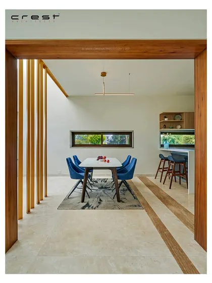 A framed view into the dining area of the 'Framed House,' showcasing a minimalist aesthetic with a pop of blue from the chairs.