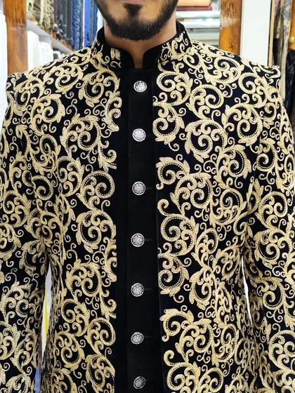 A close-up of a black and gold embroidered open sherwani, showing the intricate details of the threadwork over a velvet inner jacket.