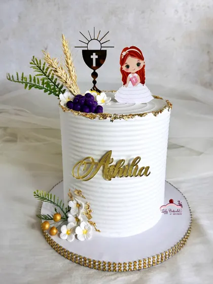 A simple and sweet first holy communion cake, with a white textured finish, gold details, and toppers representing wheat and grapes.