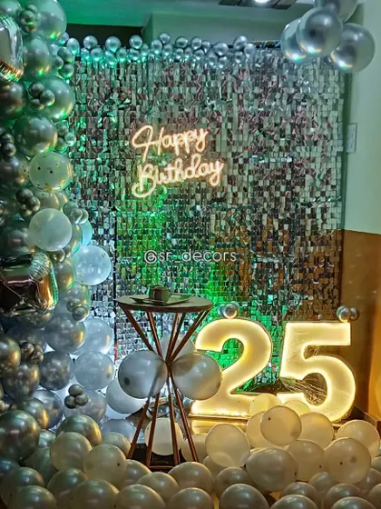 A 25th birthday celebration with a silver shimmer wall, a silver and white balloon garland, and a glowing light-up '25'.