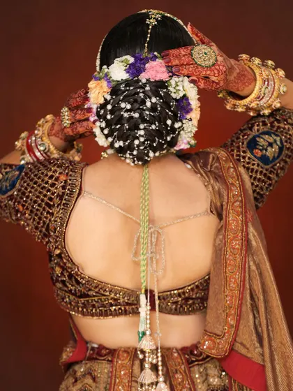 A back view of a classic bridal updo. The bun is intricately woven and adorned with a mix of colorful flowers and delicate pearl strings, showcasing our attention to detail.