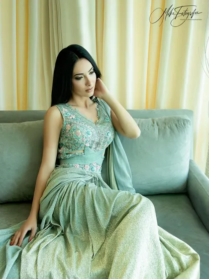 A relaxed, elegant portrait of a model in a light green gown, shot on location. The soft, natural lighting from the window creates a serene and sophisticated mood.