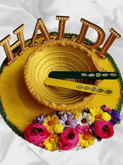 A personalized Haldi platter that truly stands out. This piece features the word 'HALDI' in pearl studded letters, a golden bowl, and a base decorated with a rainbow of colorful flowers.