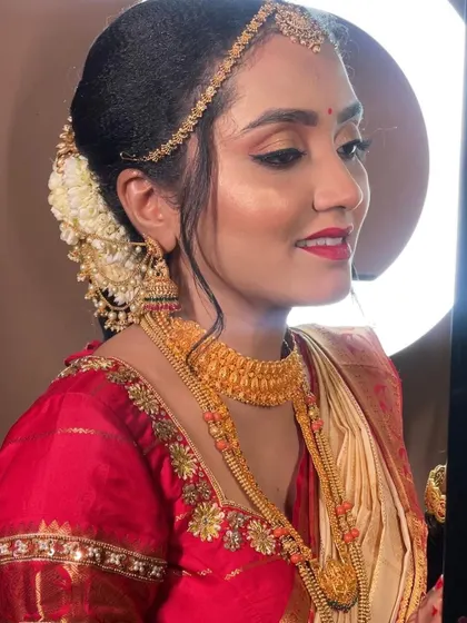A side profile showcasing the complete Muhurtham look. You can see the elegant hair bun adorned with flowers, the glow on her skin, and how the gold jewellery perfectly complements the makeup.