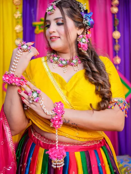 A vibrant Mehendi look! The bride is glowing in her colorful rainbow lehenga and floral jewelry, with makeup that is fresh and fun.