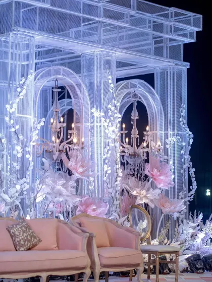 A detail shot of the stage seating, highlighting the delicate pink velvet chairs and the intricate white structures adorned with custom paper flowers and classic chandeliers, creating a fairytale-like setting.