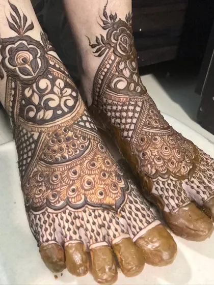 A close-up of a bridal foot design, featuring peacock motifs and delicate dot work.