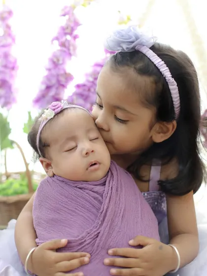 A gentle kiss for a sleeping baby. This shot, coordinated in soft lavender, highlights the sweet and protective nature of an older sister.