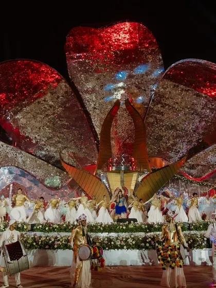 A grand stage production with dozens of performers, drummers, and a massive, shimmering floral backdrop. This is wedding entertainment on a theatrical scale.