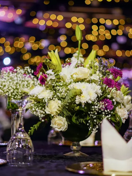 A beautiful floral centerpiece on a dining table, with the bokeh of event lights in the background creating a magical, festive atmosphere.
