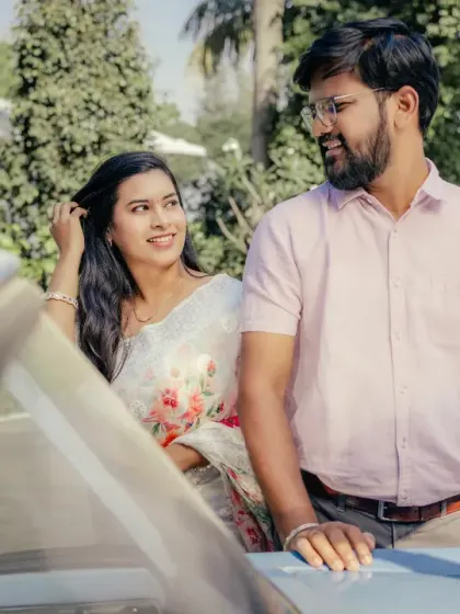 Capturing the candid, in-between moments of a pre-wedding shoot. The couple shares a natural glance next to a vintage car, creating a relaxed and authentic photograph.