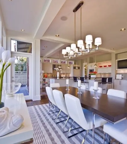 A bright and modern dining area connected to an open kitchen, featuring a Buddha statue for a touch of tranquility and large windows for an indoor-outdoor feel.