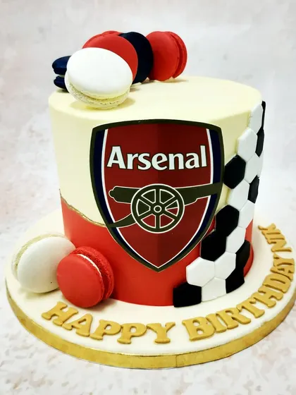 We show team pride with this sharp Arsenal FC themed cake. The iconic club crest is the centerpiece, set against the team's red and white colors, with a football pattern and macarons completing this stylish design for a true Gooner.