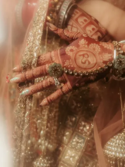 A close-up on the bride's hands, showcasing the intricate henna design with the couple's initials, a beautiful and personal detail.