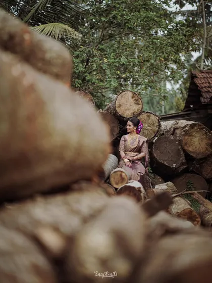 A creative shot of the bride seated amongst stacked logs, creating a unique contrast between rustic nature and bridal elegance.