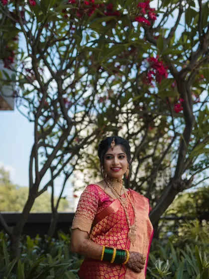 The bride framed by a flowering tree, looking radiant in her traditional South Indian style saree, showcasing our versatility in capturing different regional looks.
