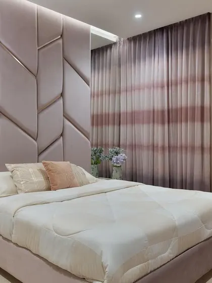 This bedroom showcases a stunning mauve-toned, geometrically upholstered headboard that extends across the wall, creating a soft yet dramatic focal point.