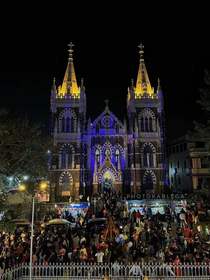 The stunning facade of Mount Mary Basilica in Bandra, illuminated with blue and yellow lights for Christmas, with crowds gathered to celebrate.