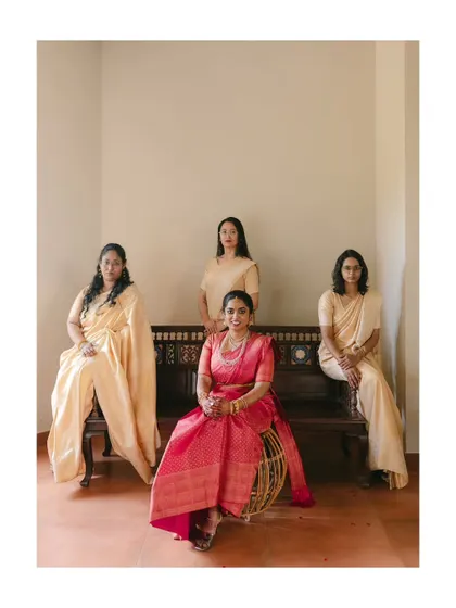 A formal portrait of the bride in a vibrant pink saree, seated with her elegantly dressed bridesmaids. The composition is classic, beautiful, and full of poise.