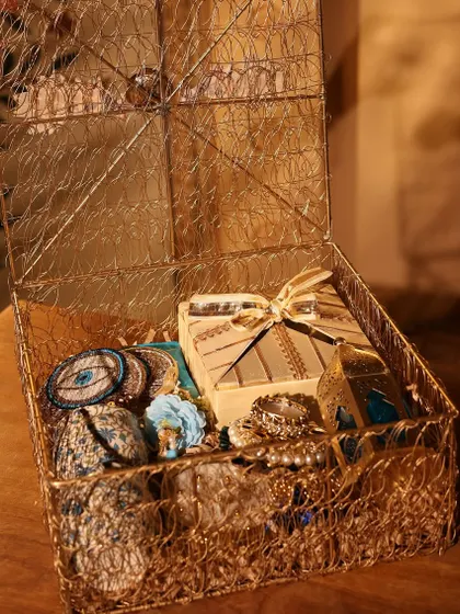 An artfully arranged golden wire box filled with a mix of traditional and contemporary items in shades of blue and gold.