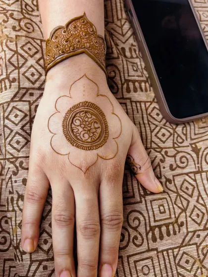 A work-in-progress shot of the mandala design, showing the fresh henna paste and the reference photo on the phone.