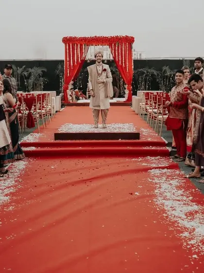 The groom's anticipation. He waits for his bride at the mandap, the red aisle stretching before him, creating a powerful and cinematic image of the moments before the union.