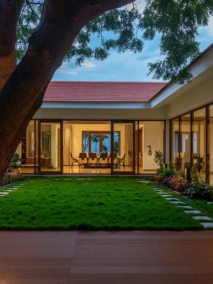 A view from the central tree in the Greenfield farmhouse courtyard, looking towards the dining room. The floor-to-ceiling glass walls create a seamless visual connection.