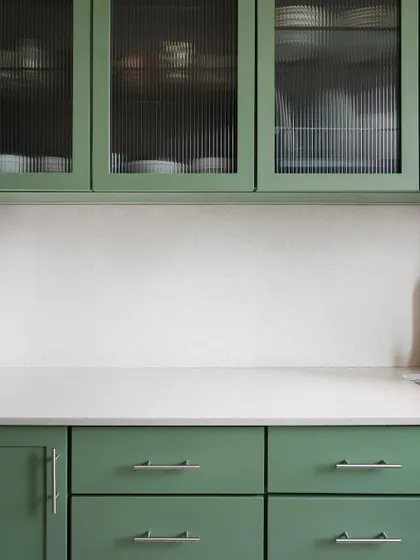A close-up of the custom green kitchen cabinets. The reeded glass in the upper cabinets adds a lovely texture and partially conceals the contents, keeping the space from feeling cluttered.