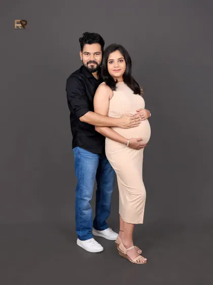 A classic couple's portrait against a simple grey backdrop. Their coordinated neutral and dark outfits create a sophisticated and modern look.