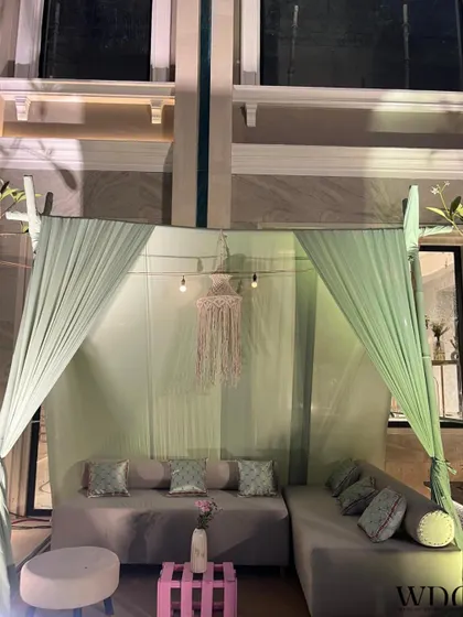 A cozy and intimate seating area, draped in soft mint green curtains and accented with a delicate macrame hanging, exuding a warm and welcoming ambiance.