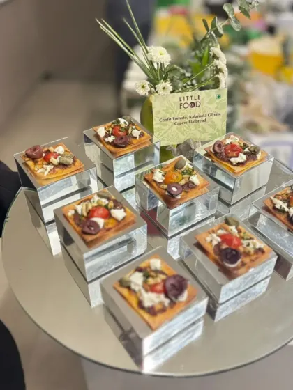 Mini flatbreads topped with sun-dried tomatoes, Kalamata olives, capers, and feta. These Mediterranean-inspired bites are served on individual mirrored blocks, adding a modern and reflective element to the presentation.