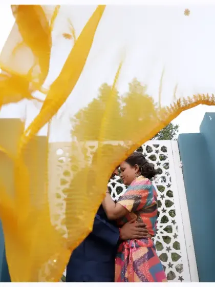 An artistic pre-wedding shot using a flowing yellow dupatta to frame the couple. This creative technique adds a pop of color and a sense of movement to the romantic embrace.