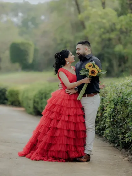 A beautiful pose during a pre-wedding session in a Pune garden. The woman's vibrant red dress stands out against the green foliage, creating a visually stunning and romantic photograph.