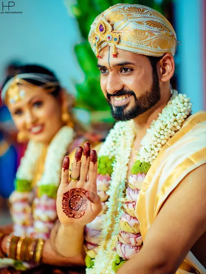A candid shot of the groom showing his henna-decorated hand, with his smiling bride beside him.