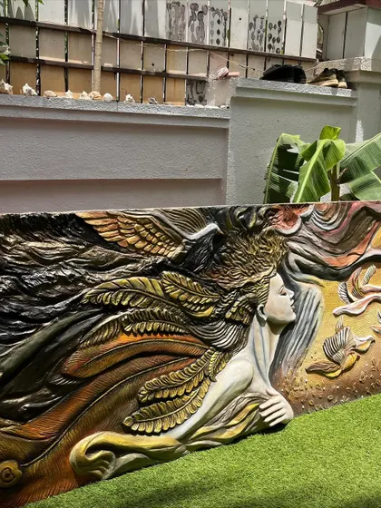 The mural photographed outdoors before installation, with natural light revealing the rich textures and details of the sculpted feathers and hair.