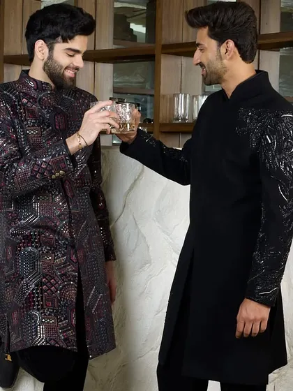 Two gentlemen sharing a toast, both in my bespoke black kurtas. One features the embroidered cheetah, while the other has a complex geometric pattern, showcasing different ways to express evening elegance.