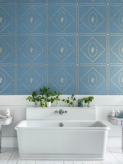 The 'Conchiglie' wallpaper from Cole & Son, featuring a geometric arrangement of shells. In this bathroom, the soft blue and metallic gold design adds a touch of coastal elegance and intricate detail.
