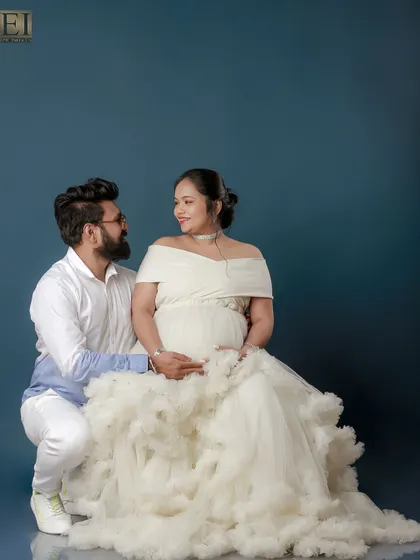 An elegant studio portrait with the couple dressed in white. The dad-to-be kneels, creating a beautiful composition that honors the mom-to-be.