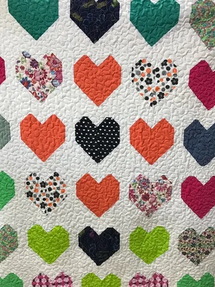 A "Clashing Hearts" quilt with a variety of colorful and patterned hearts on a white background.