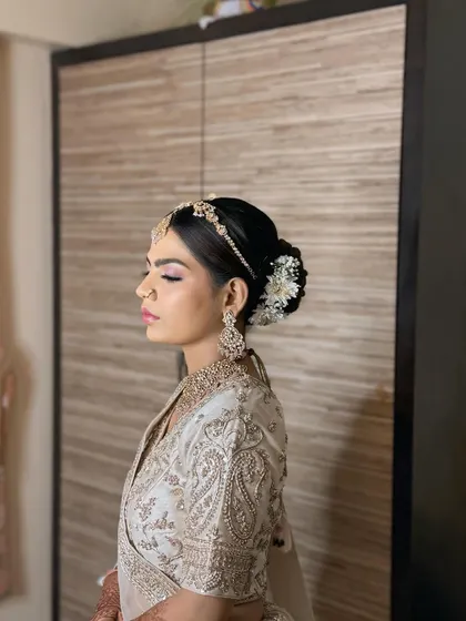 A side view of Maya's look, highlighting her classic floral bun and the delicate embroidery on her white lehenga.