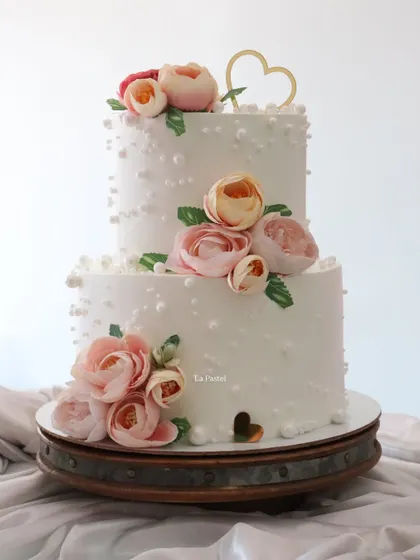 A sweet and romantic two-tier engagement cake. The design features delicate pearl-like dots and is adorned with beautiful pink sugar flowers for a classic and elegant feel.