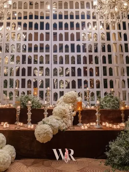A unique decor element featuring a wall of white arched mirrors, creating an interesting visual texture. In front, a cascade of white floral spheres and candles adds a touch of modern artistry.