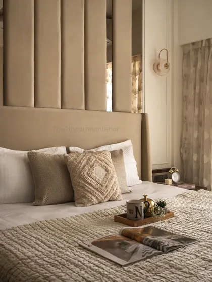 A close-up of the bed styling, showcasing the layered textures of the knitted bedspread and throw pillows. Details like the personalized mug and open magazine invite relaxation and add a personal touch.