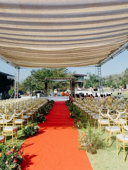 The long aisle, covered with a vibrant red carpet, leads guests' eyes directly to the beautiful floral mandap. The seating is arranged to ensure every guest has a perfect view of the ceremony.